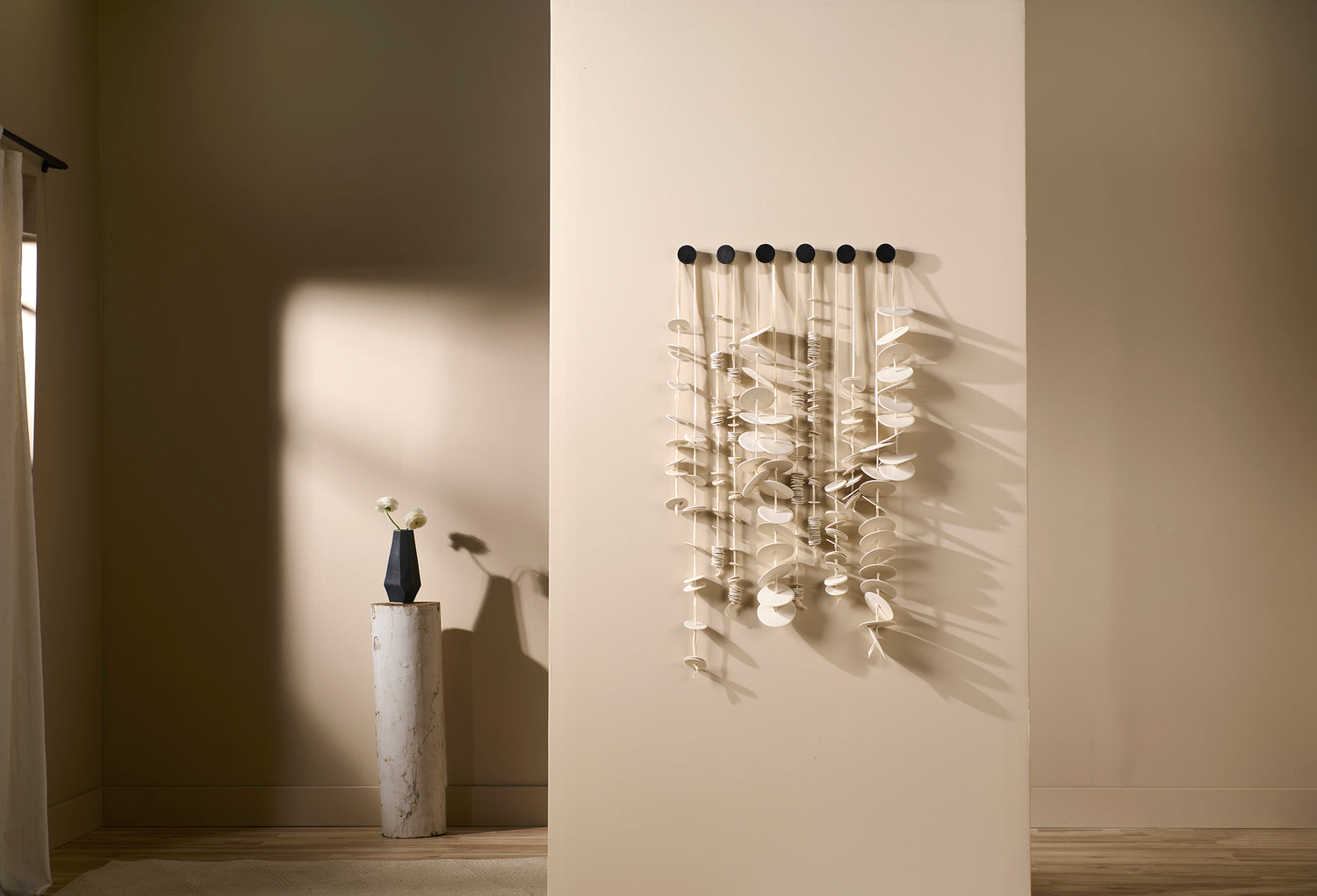 Vertical porcelain wall sculpture Cadence 6 by Lauren HB Studio displayed in a minimal interior. Six strands of hand-formed porcelain discs hang in rhythmic formation.