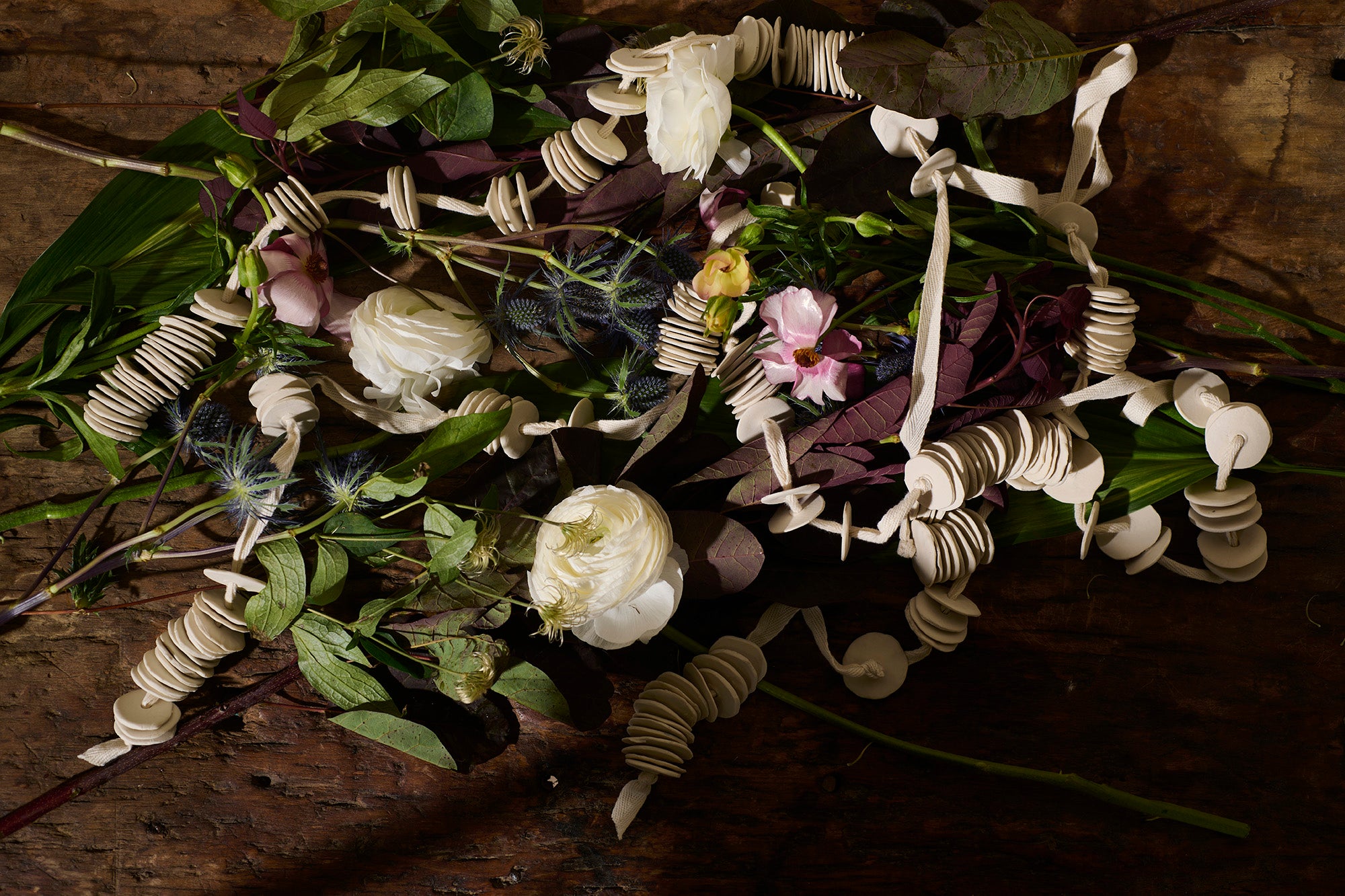Floral arrangement intertwined with handcrafted porcelain discs by Lauren HB Studio, blending nature and sculpture on a rustic wooden surface.