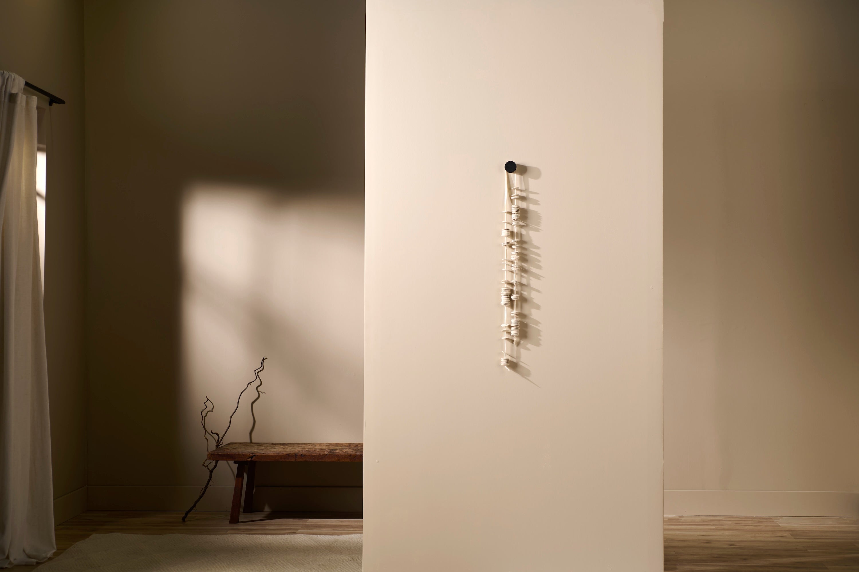 Handcrafted porcelain wall sculpture titled Cadence 1 by Lauren HB Studio, shown suspended against a neutral wall with wood bench in background.
