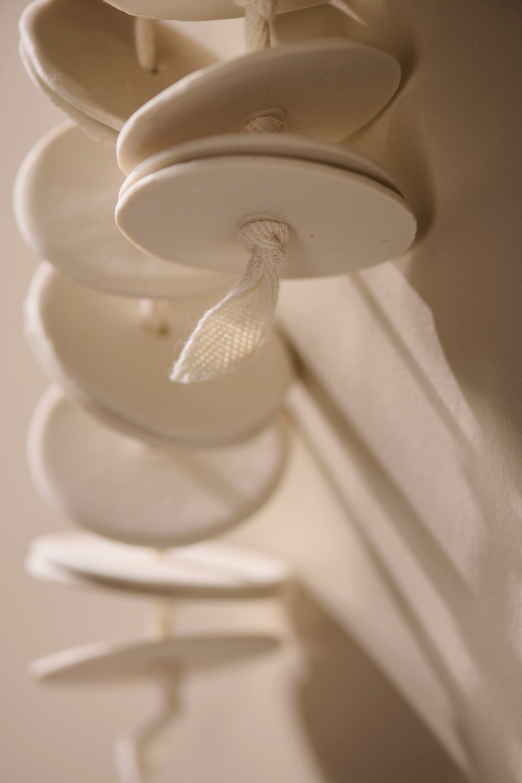 Close-up of Cadence 2 showing layered porcelain discs threaded on twill tape. Highlights subtle irregularities, raw porcelain texture, and the craftsmanship of hand-formed design.