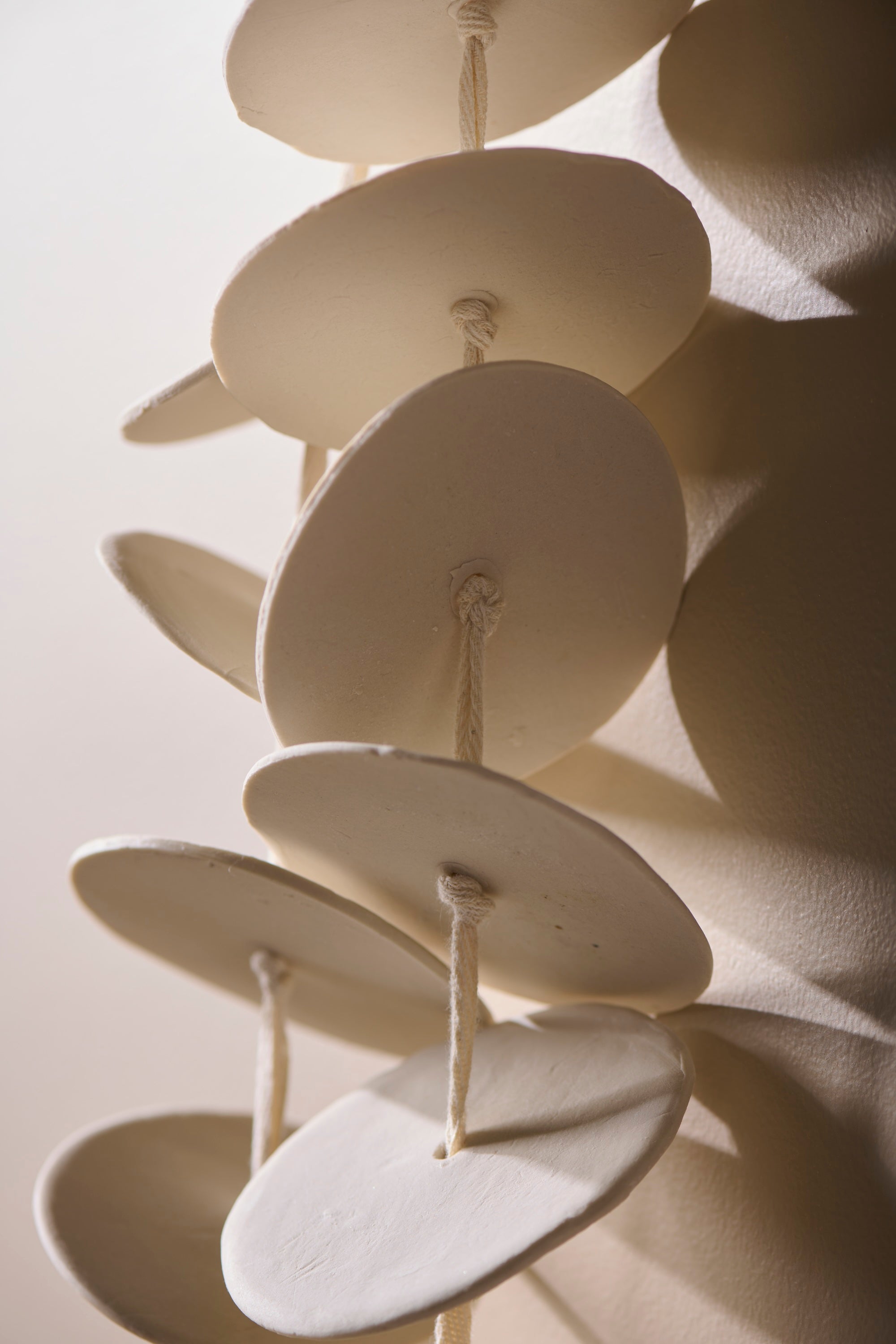 Close-up of Cadence 3 showing stacked porcelain discs strung on twill tape. Highlights the organic shapes and raw porcelain texture.