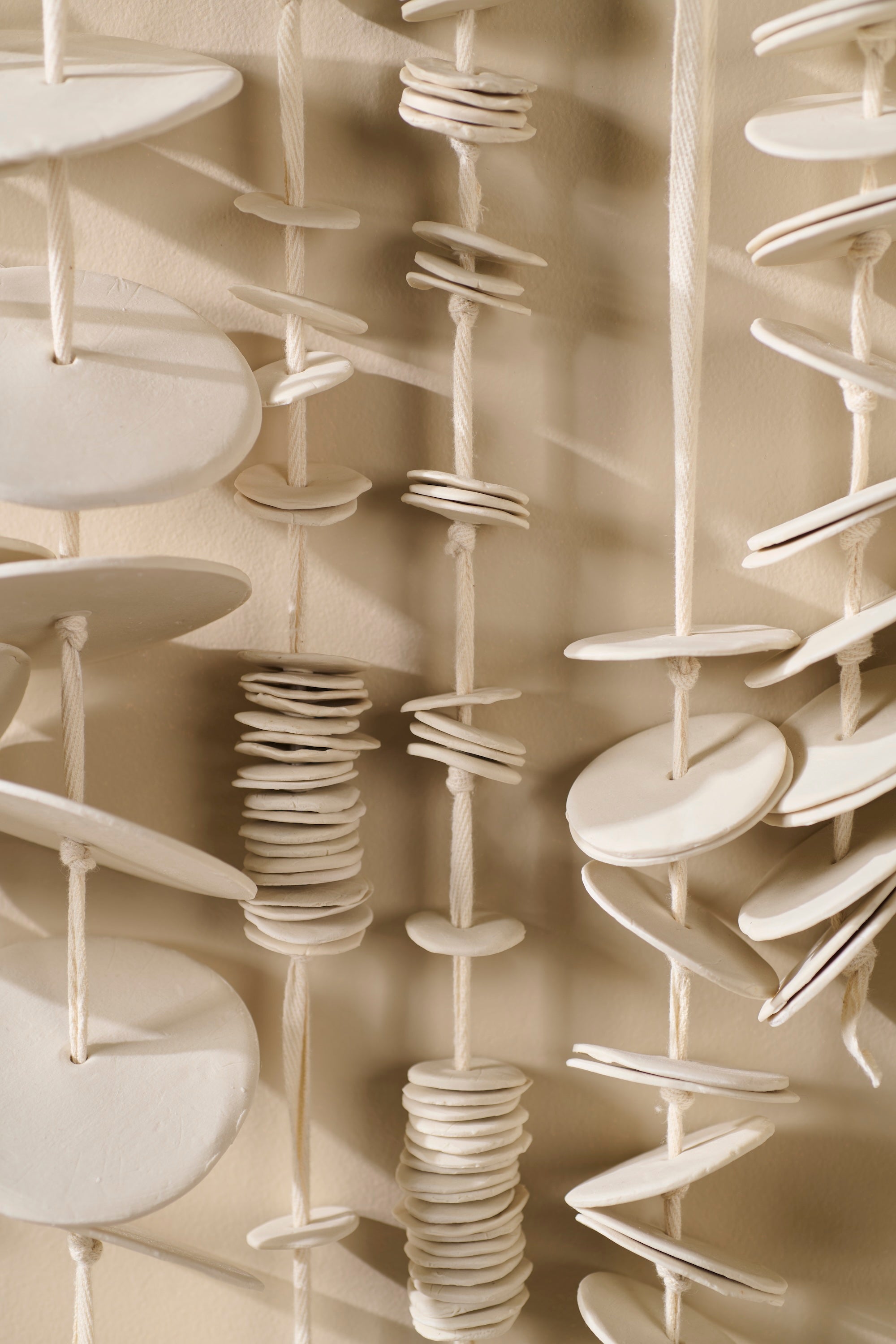 Close-up view of Cadence 6 showing layered porcelain discs strung on twill tape. Highlights craftsmanship, texture, and organic variation in each handmade piece.