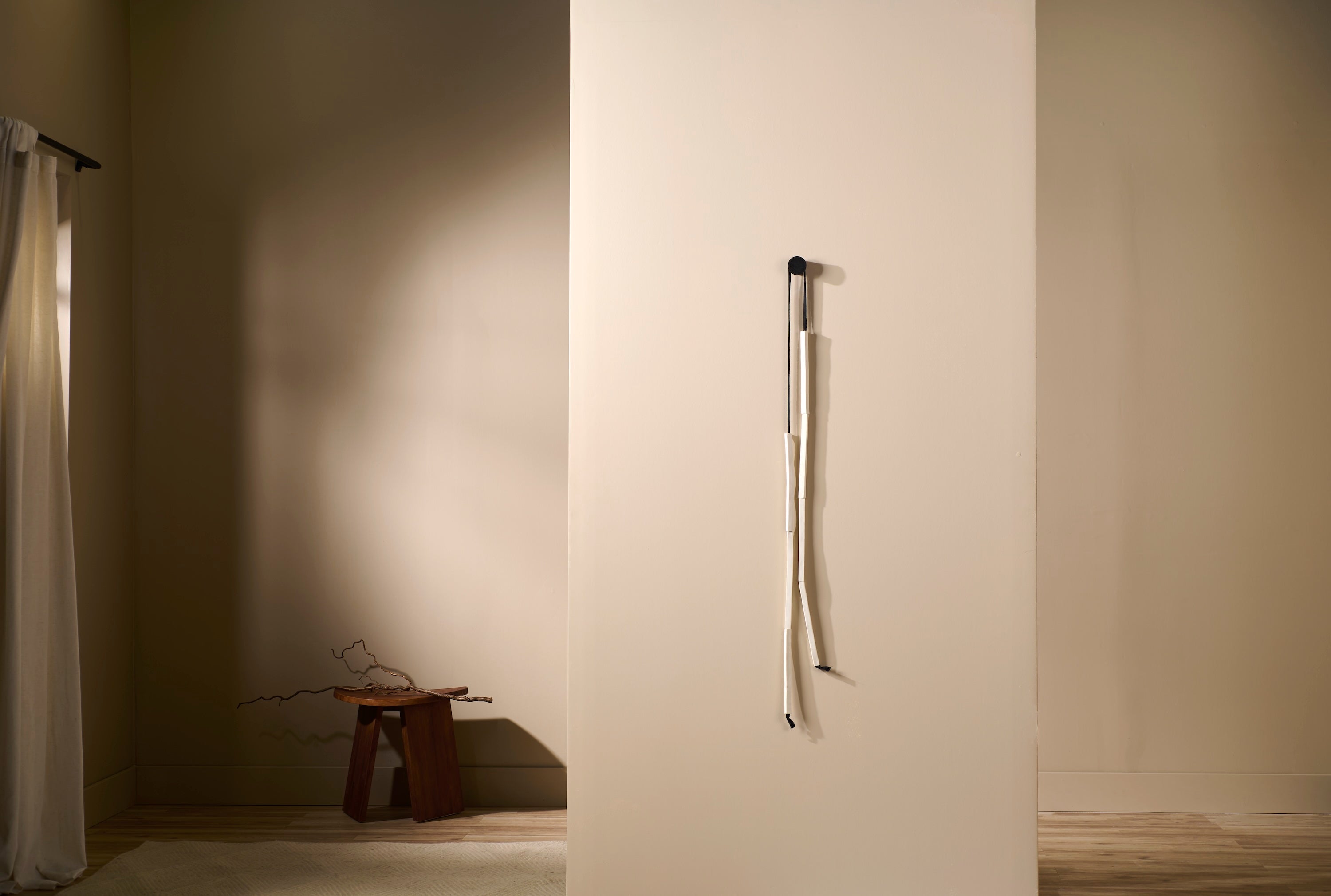 Minimal porcelain wall sculpture Counterpoint 1 by Lauren HB Studio displayed on a neutral wall. A single strand of porcelain rods suspended from a black knob creates an elegant vertical form.