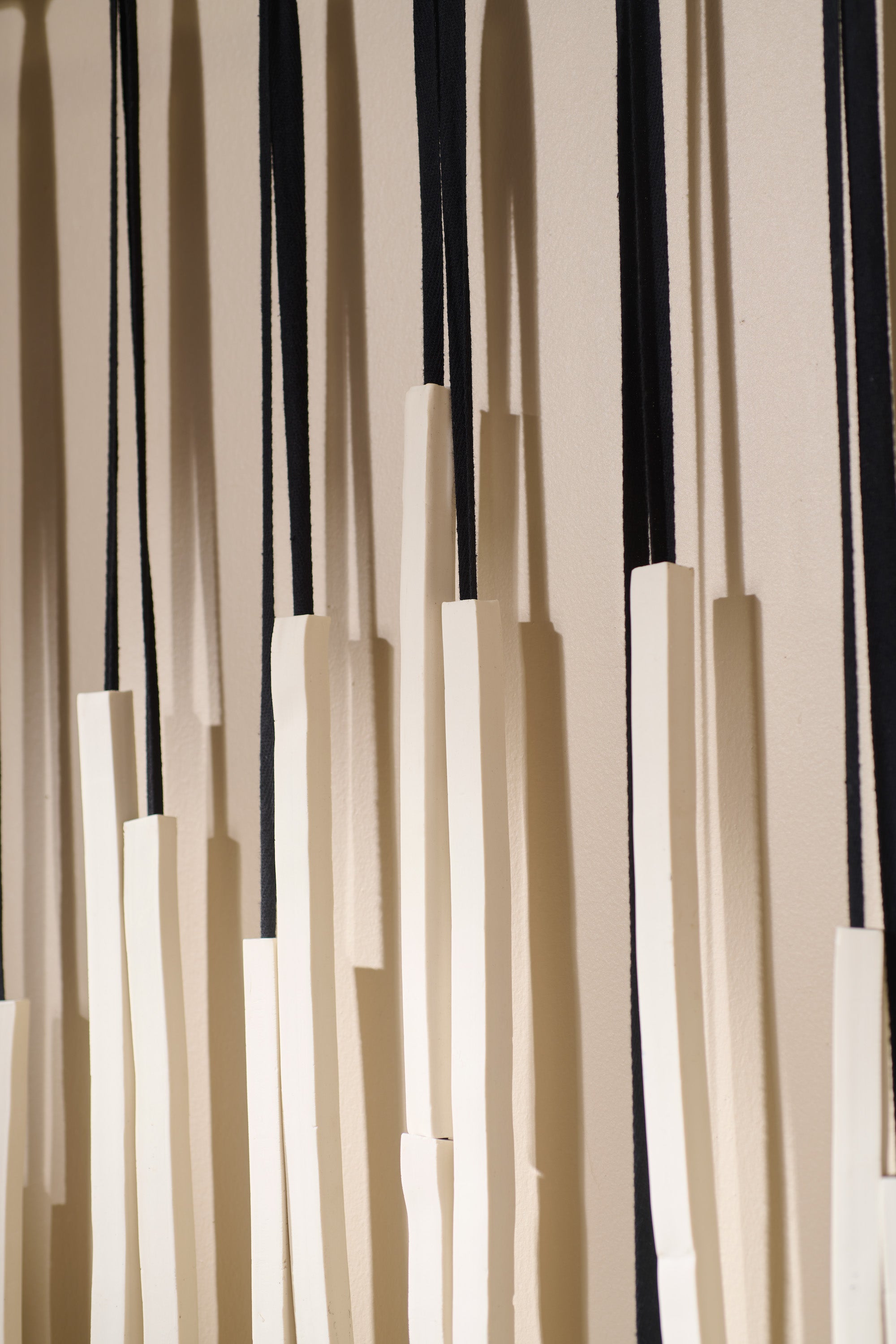 Detail view of Counterpoint 2 showing hand-formed porcelain rods strung on twill tape and hung from custom blackened hardware. Highlights the raw, tactile surface.