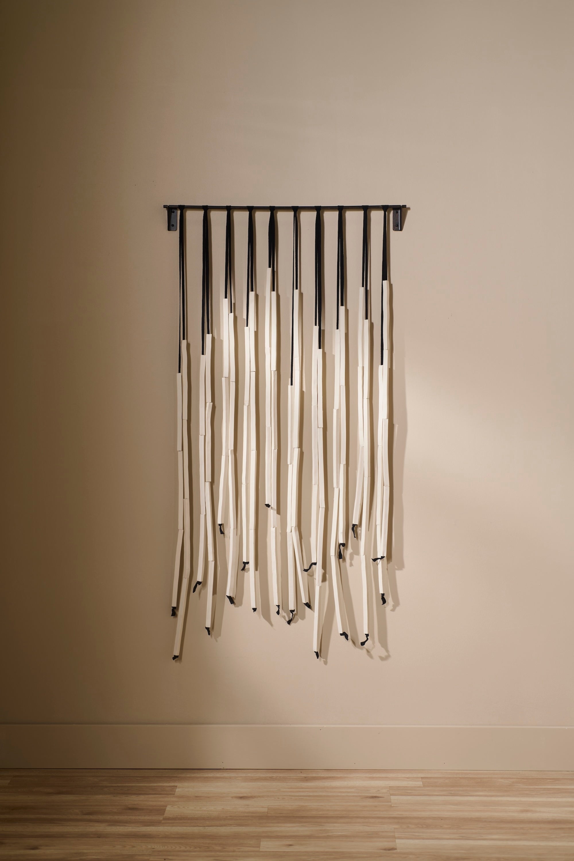 Counterpoint 2 by Lauren HB Studio — a handmade porcelain wall sculpture with unglazed porcelain rods suspended from a black metal bar on twill tape, displayed in a neutral interior.