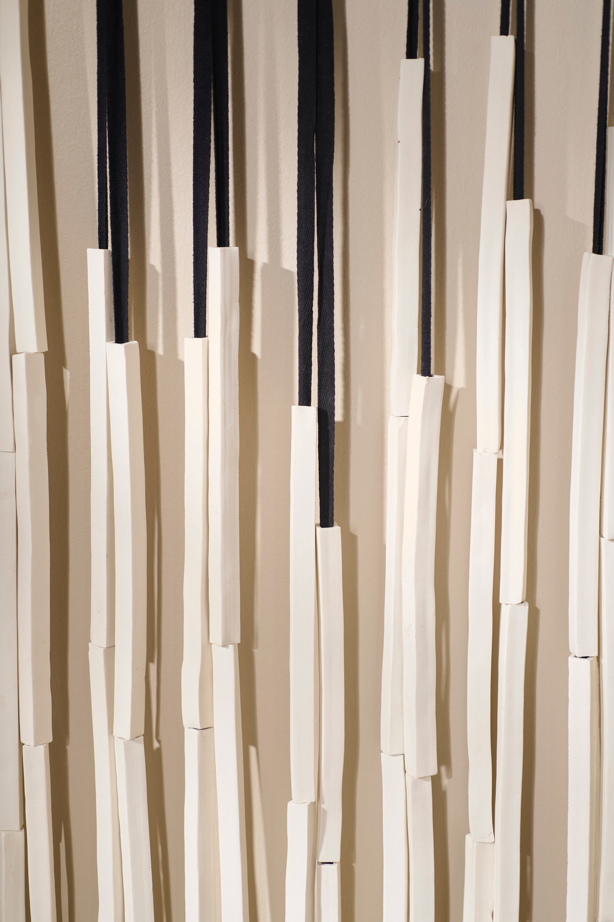 Detail of Counterpoint 3 showing porcelain rods strung vertically on twill tape. Highlights the interplay of light, shadow, and texture against the neutral backdrop.