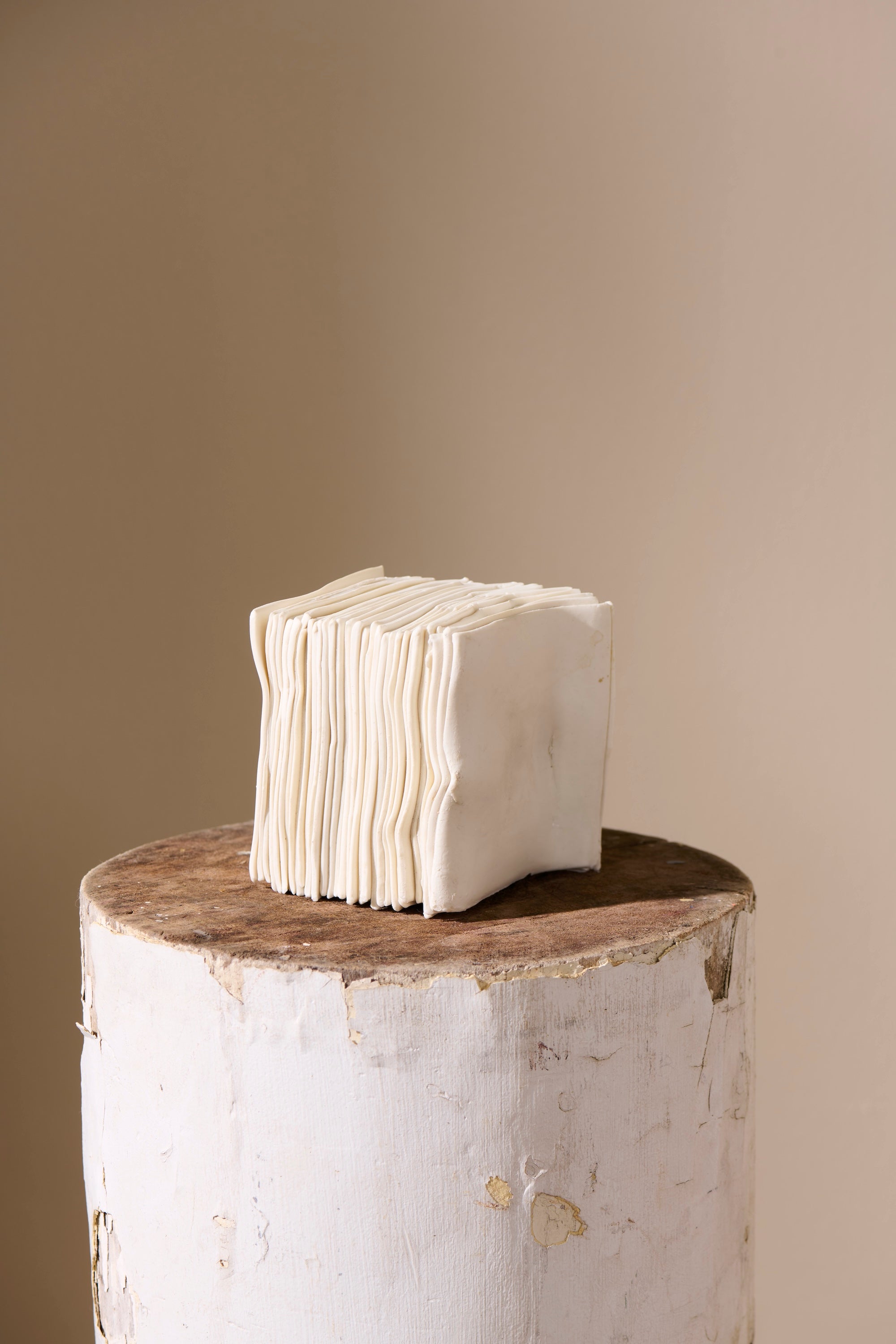Stack 11 porcelain sculpture by Lauren HB Studio — vertical stack of unglazed ceramic forms on a white pedestal, lit against a neutral wall.