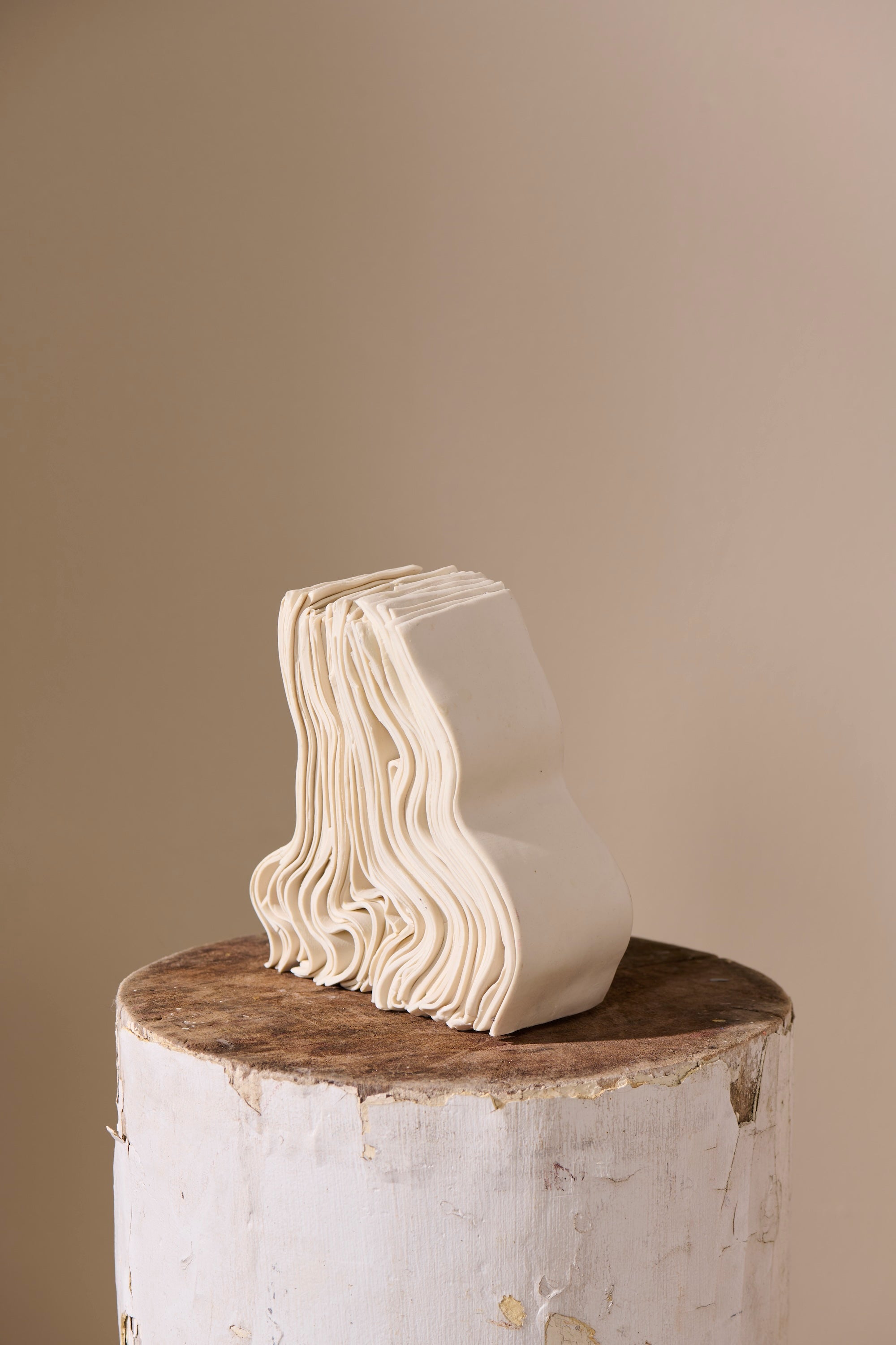 Stack 41 porcelain sculpture by Lauren HB Studio — vertical column of hand-shaped porcelain elements stacked on a white wood pedestal against a neutral wall, echoing natural cairns.