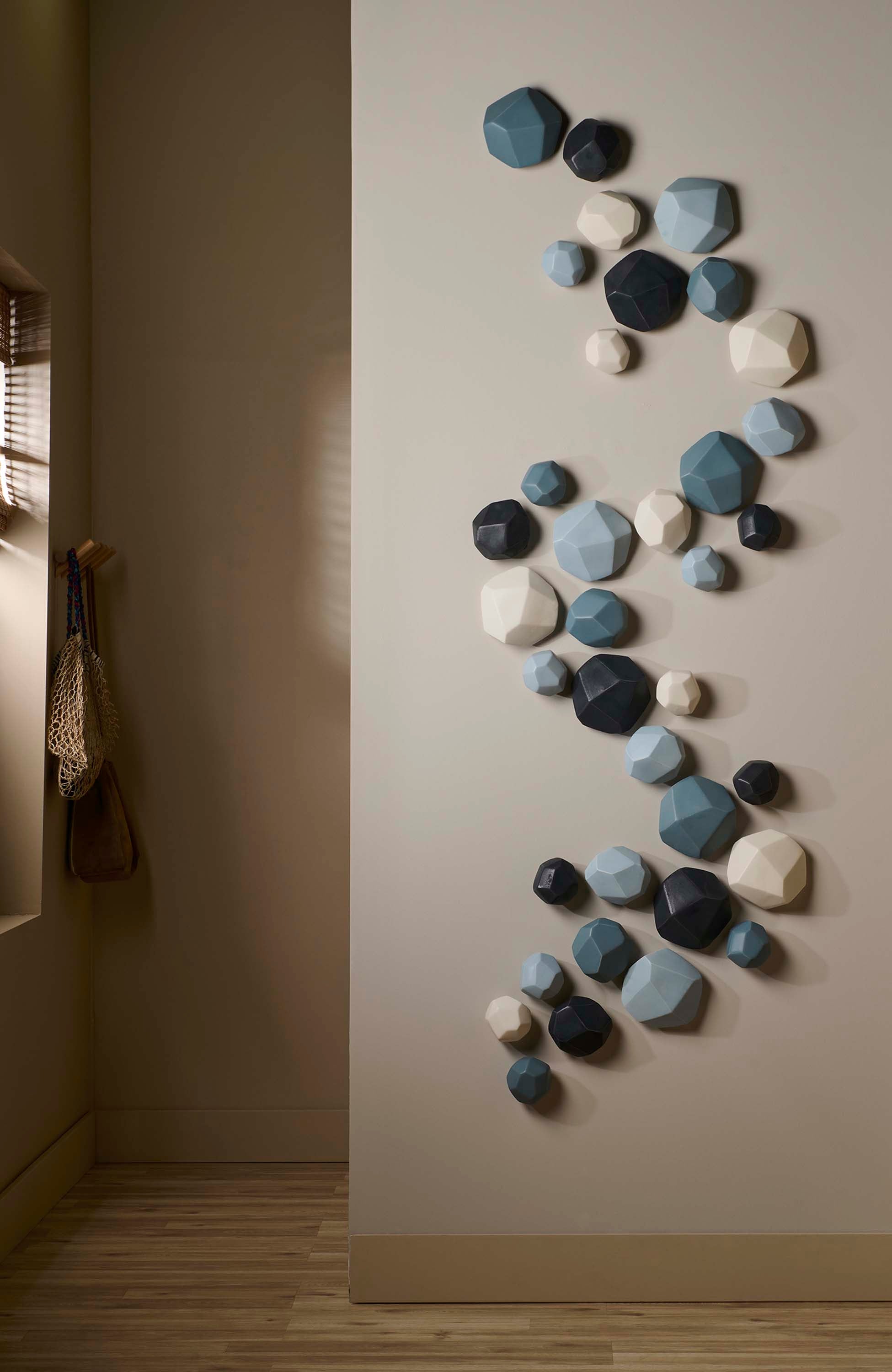 Wall Stones Set of 36 by Lauren HB Studio — porcelain stones in blue, white, and black glazes cascading down a neutral wall in soft natural light.