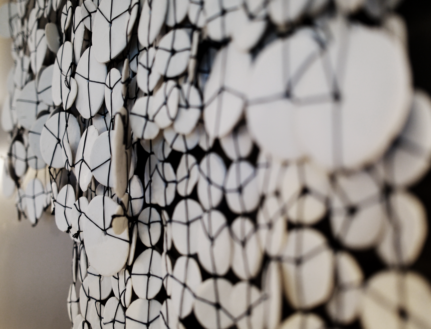 Close-up of Woven sculpture handmade with porcelain discs connected by thread, revealing subtle glaze variations and organic texture by Lauren HB Studio.